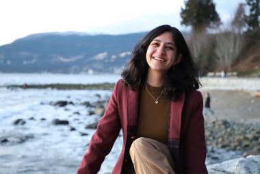 开云体育要一倍流水UBC材料工程专业的学生Gauri Taneja坐在海滩上，对着镜头微笑，远处是海洋和山脉。