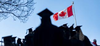 蓝色天空下的加拿大国旗，前景是一个穿着毕业礼服和帽子的学生的影子。