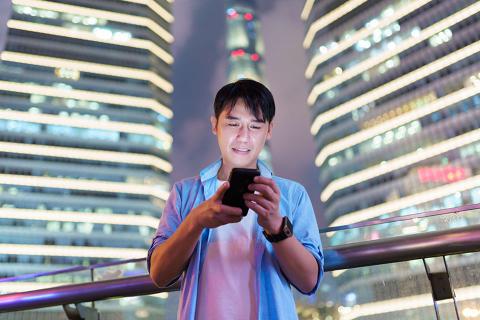 一个人站在三栋灯火通明的高楼前，看着他的手机屏幕